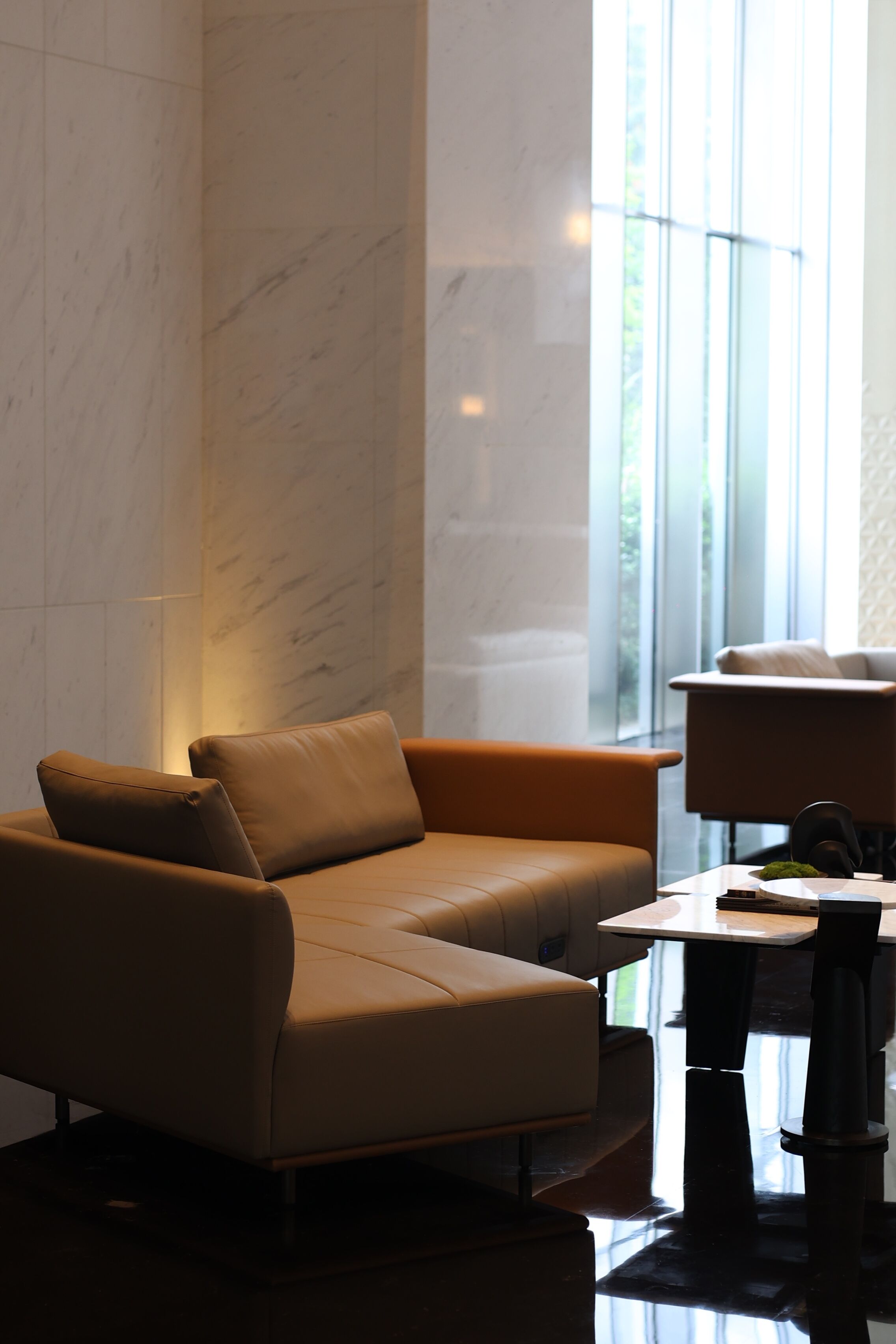 Una habitación de hotel moderna con un sofá de cuero, una mesita y vistas a zonas verdes a través de amplios ventanales.