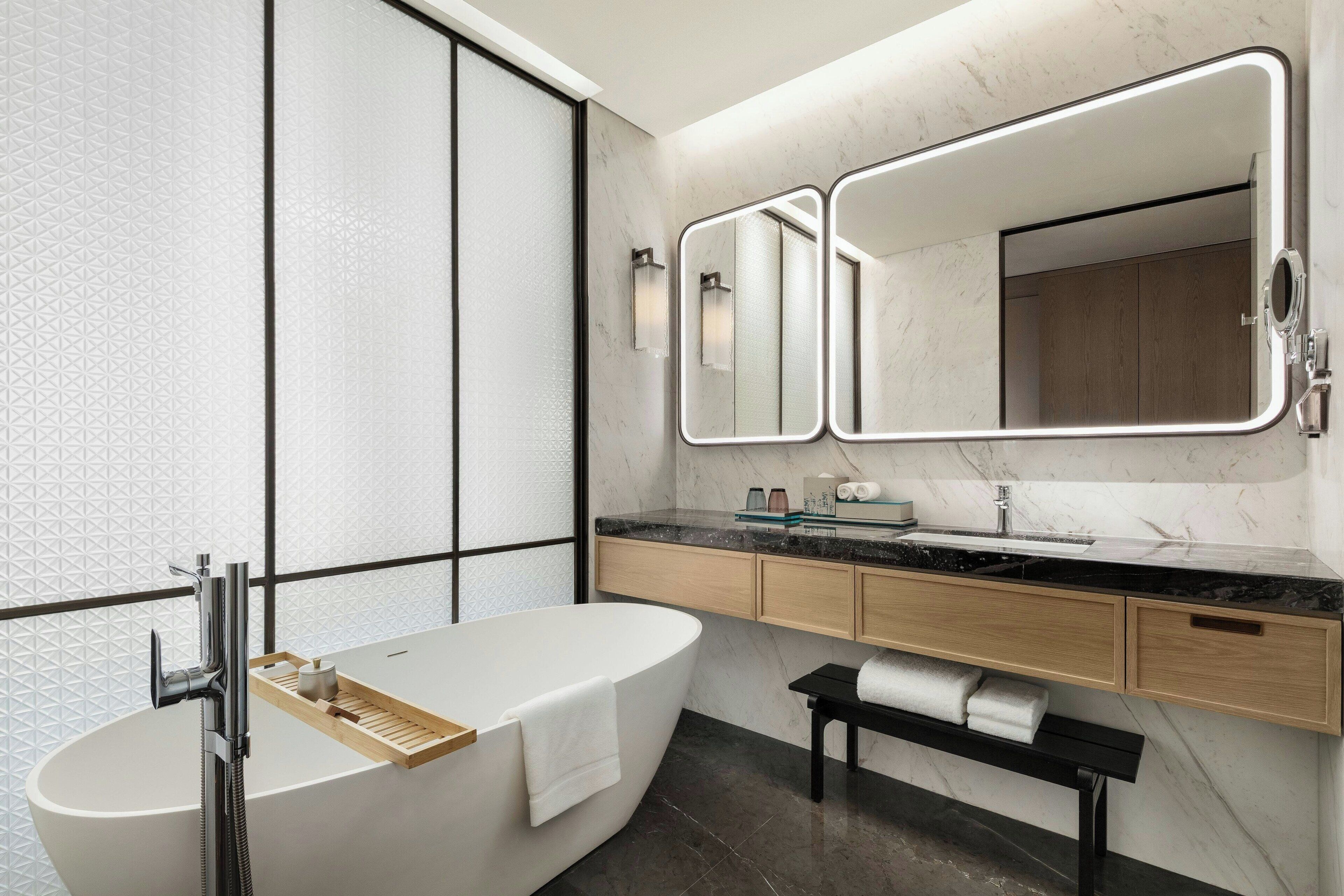 A modern bathroom with a freestanding bathtub, a vanity with a mirror, and a bench.