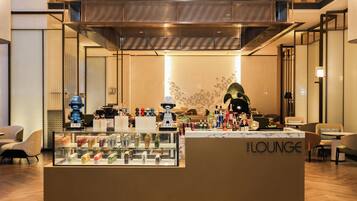 Un espace lounge moderne comprenant un présentoir en verre pour les boissons, un coin salon et un mur décoratif agrémenté d’un luminaire original.
