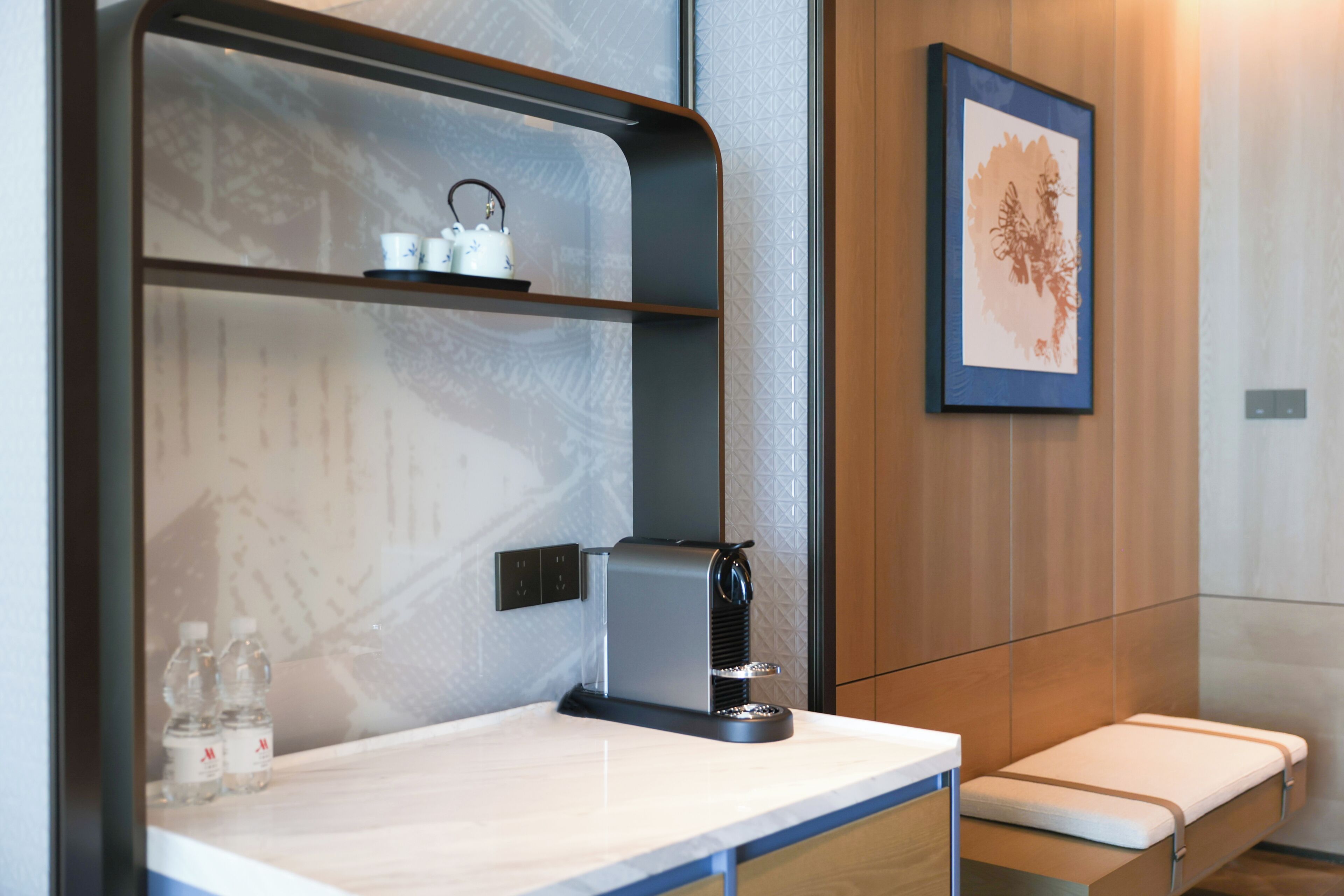 Un baño moderno con cafetera integrada, estante con artículos de tocador y una obra de arte enmarcada en la pared.