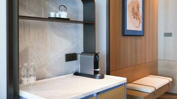 Un baño moderno con cafetera integrada, estante con artículos de tocador y una obra de arte enmarcada en la pared.