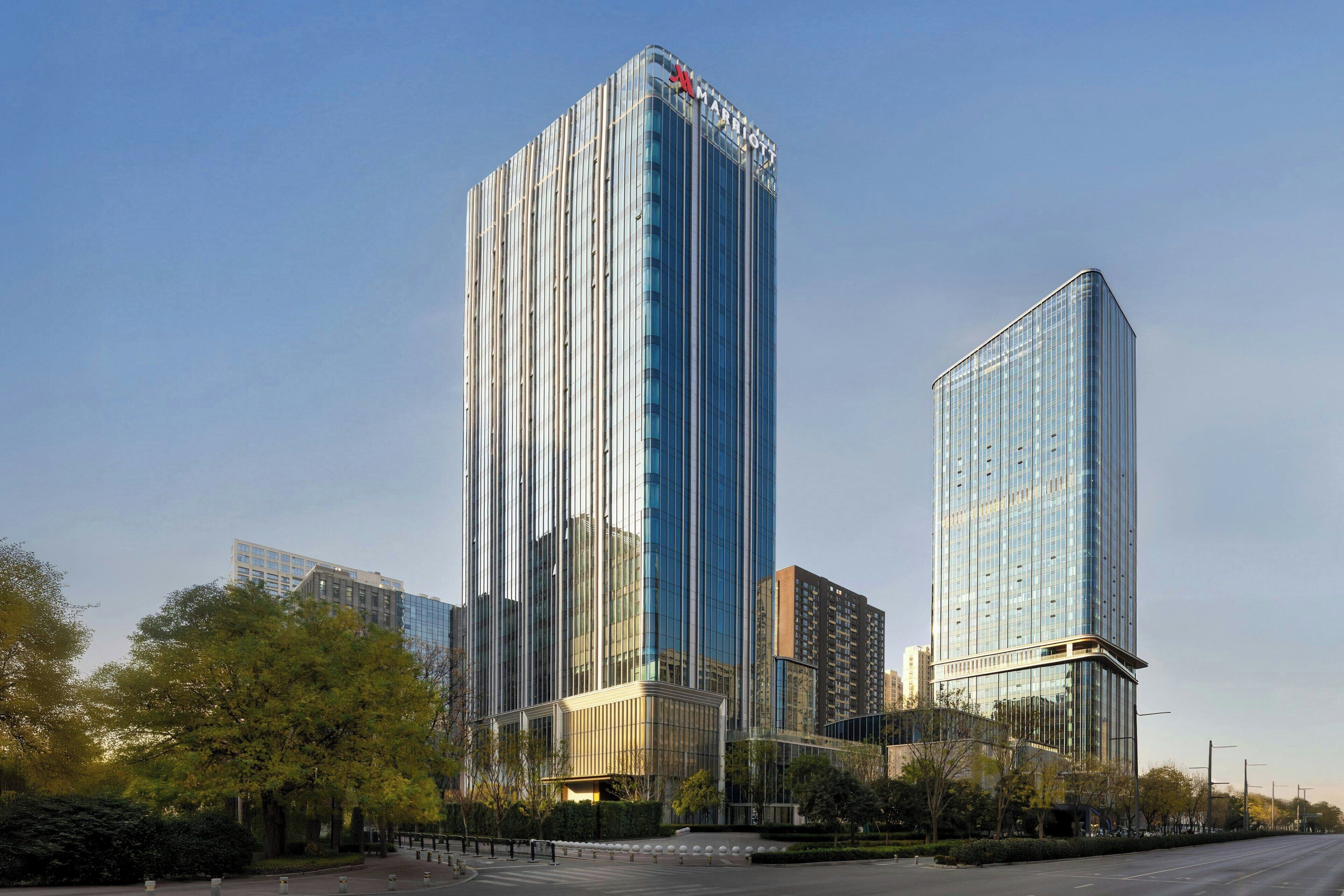 A modern high-rise building with a reflective glass facade, surrounded by trees and a clear sky.