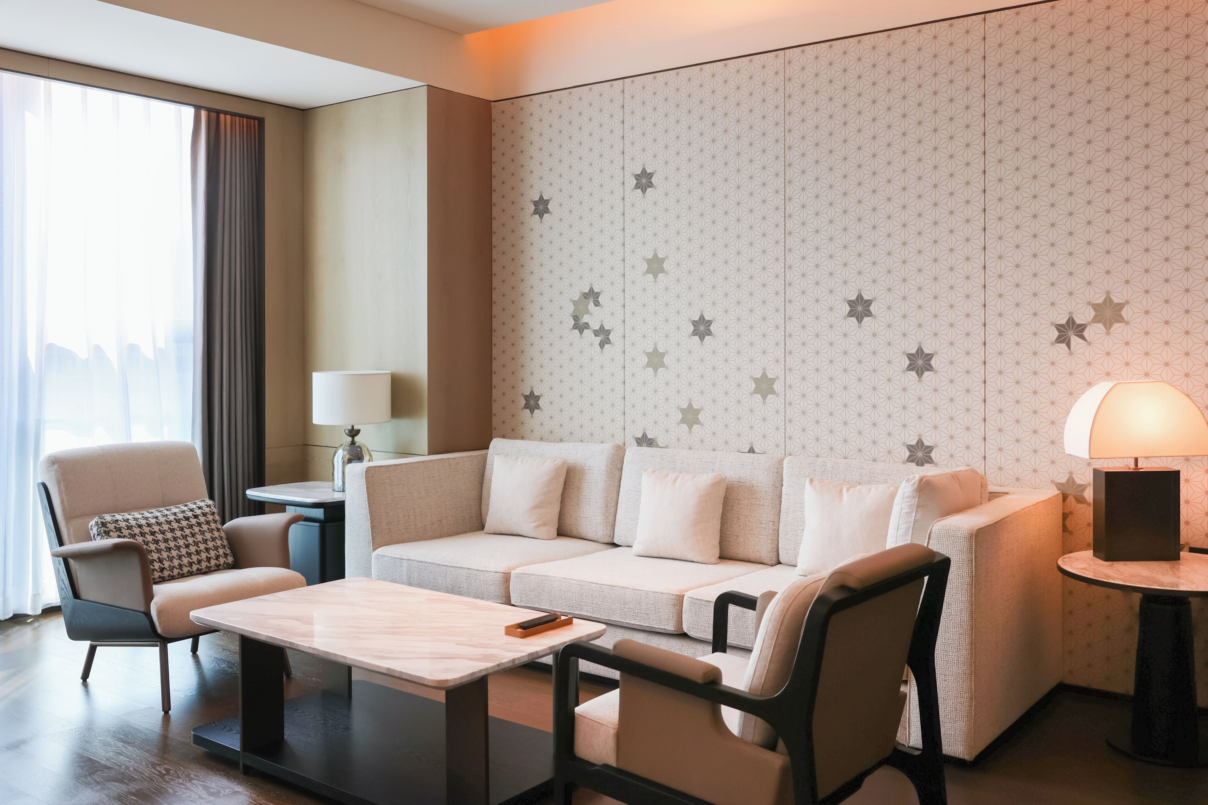 A modern hotel room with a sofa, armchairs, a small table, and a lamp.
