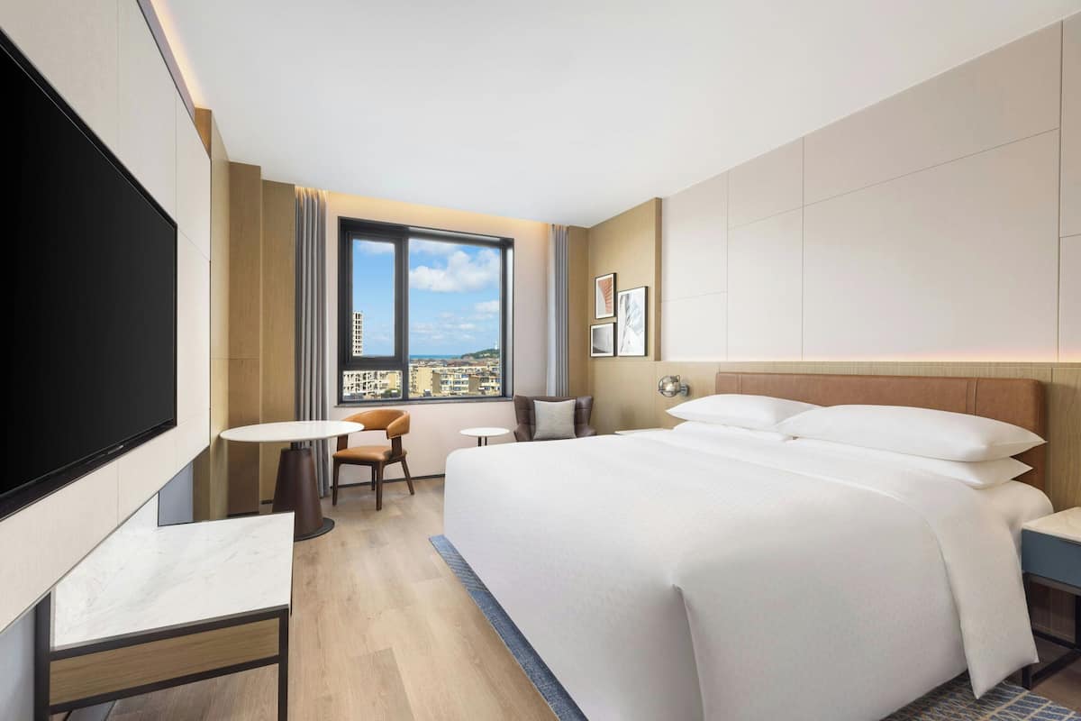 Een hotelkamer met een groot bed, een bureau, een stoel, een flatscreen televisie en uitzicht op de stad.