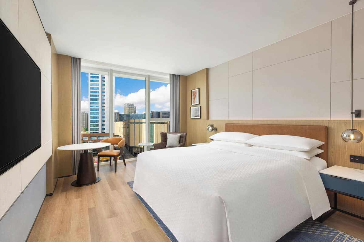 Een hotelkamer met een groot bed, een bureau, een stoel, een televisie en uitzicht op de stad.
