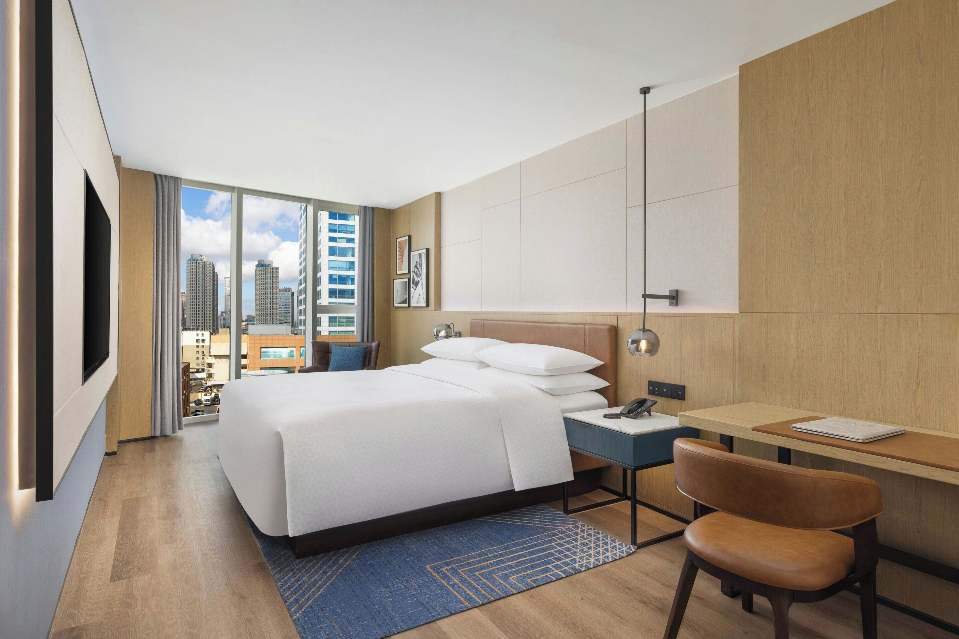 Habitación de hotel con una cama grande, un escritorio, una silla, vistas a la ciudad y un diseño moderno.