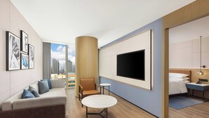 Une chambre d’hôtel moderne équipée d’un canapé, d’une table ronde, d’un téléviseur fixé au mur et d’un lit avec une table de chevet.