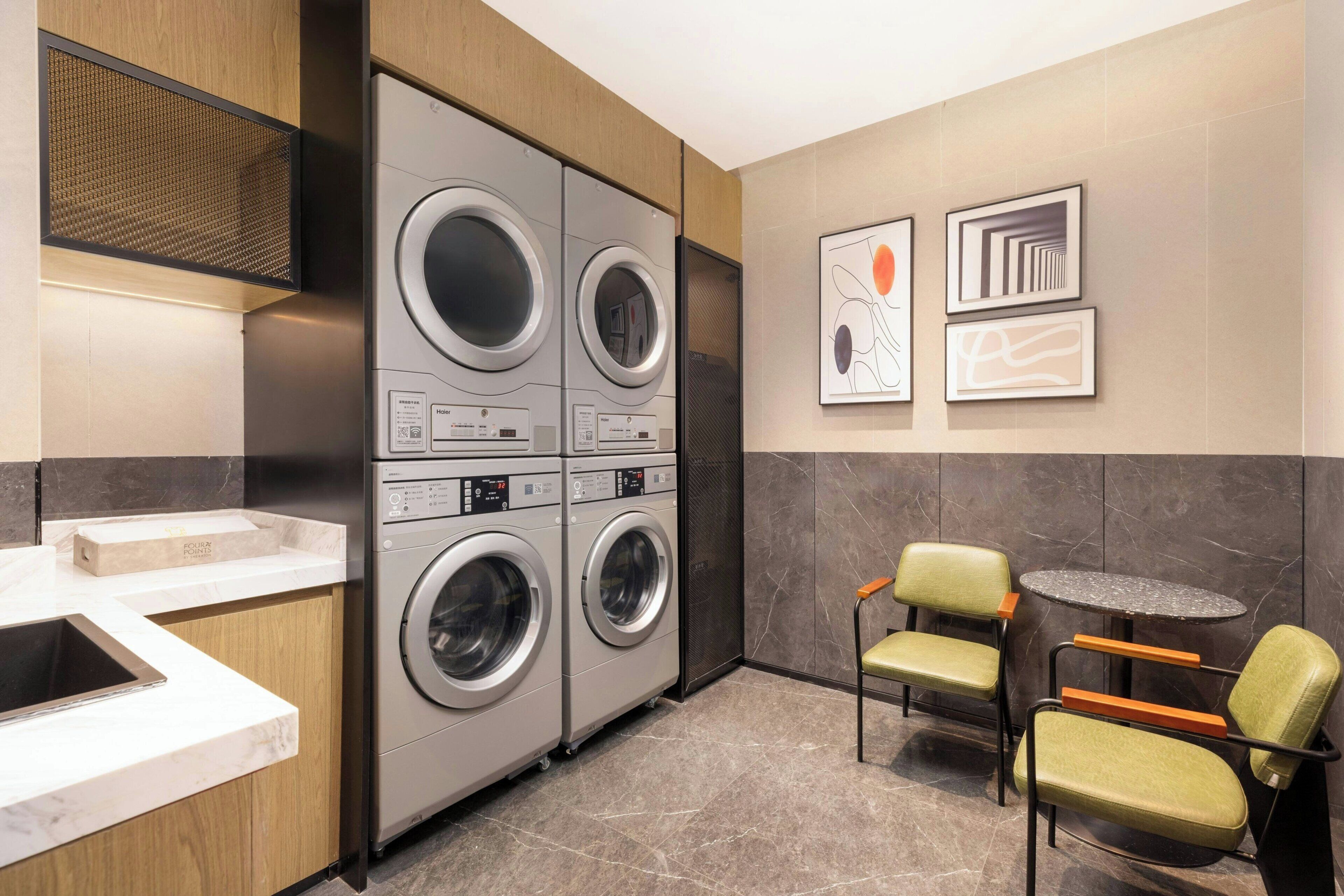 A modern laundry room with four stacked washing machines, a sink, and two chairs.