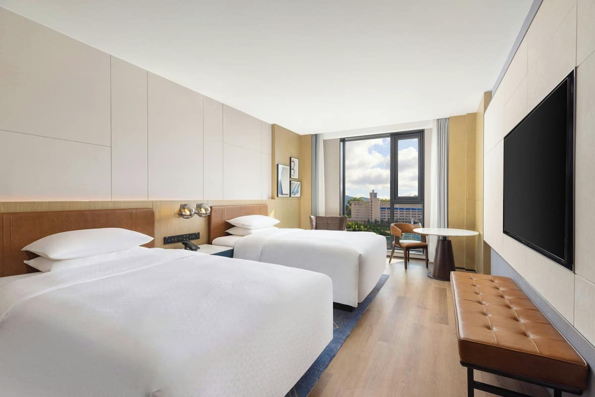 Een hotelkamer met twee bedden, een bureau, een stoel, een televisie en een groot raam.