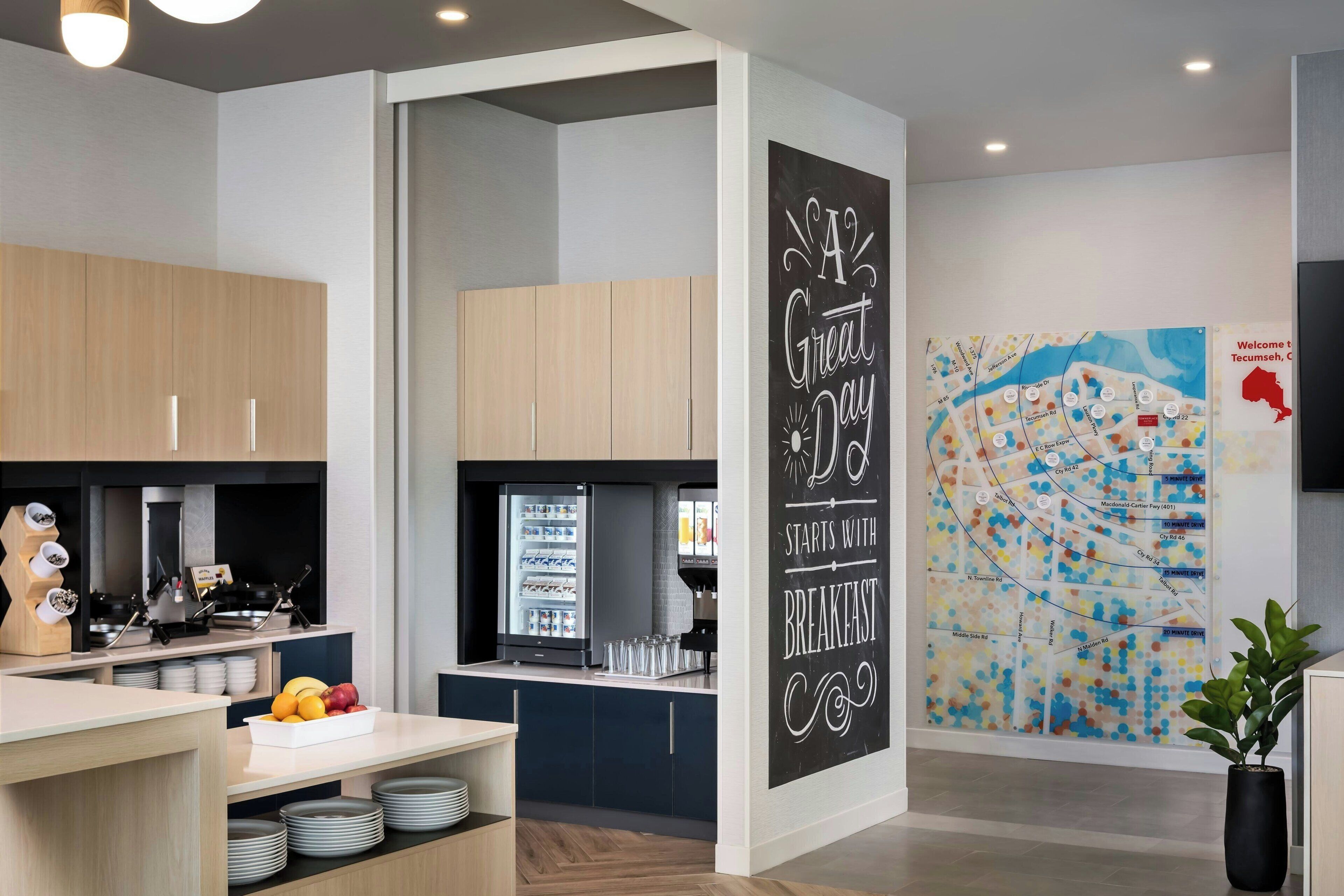A modern kitchen with wooden cabinets, a refrigerator, and a breakfast bar. There is a wall with a map and a sign that says "A Great Day Starts with Breakfast."