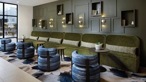 A modern lounge area with a green sofa, blue patterned ottomans, and wall-mounted lighting. - Springhill Suites By Marriott High Point Downtown (High Point)