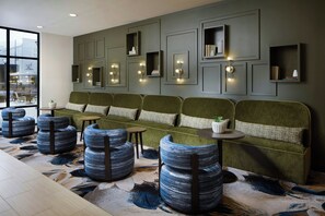 A modern lounge area with a green sofa, blue patterned ottomans, and wall-mounted lighting. - Springhill Suites By Marriott High Point Downtown (High Point)