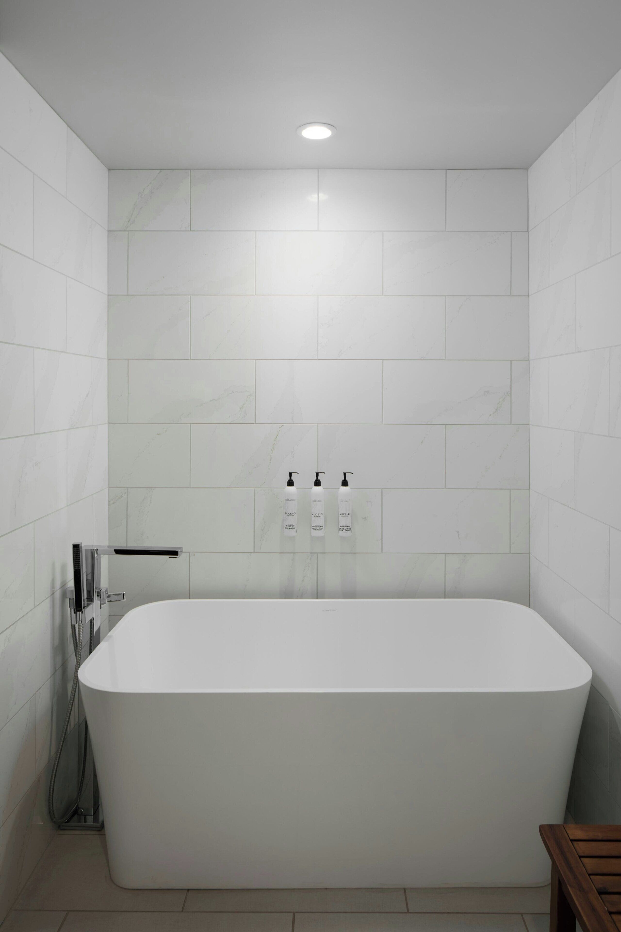 Une salle de bain moderne avec une baignoire sur pieds, des carreaux blancs et deux bouteilles de shampoing accrochées au mur.