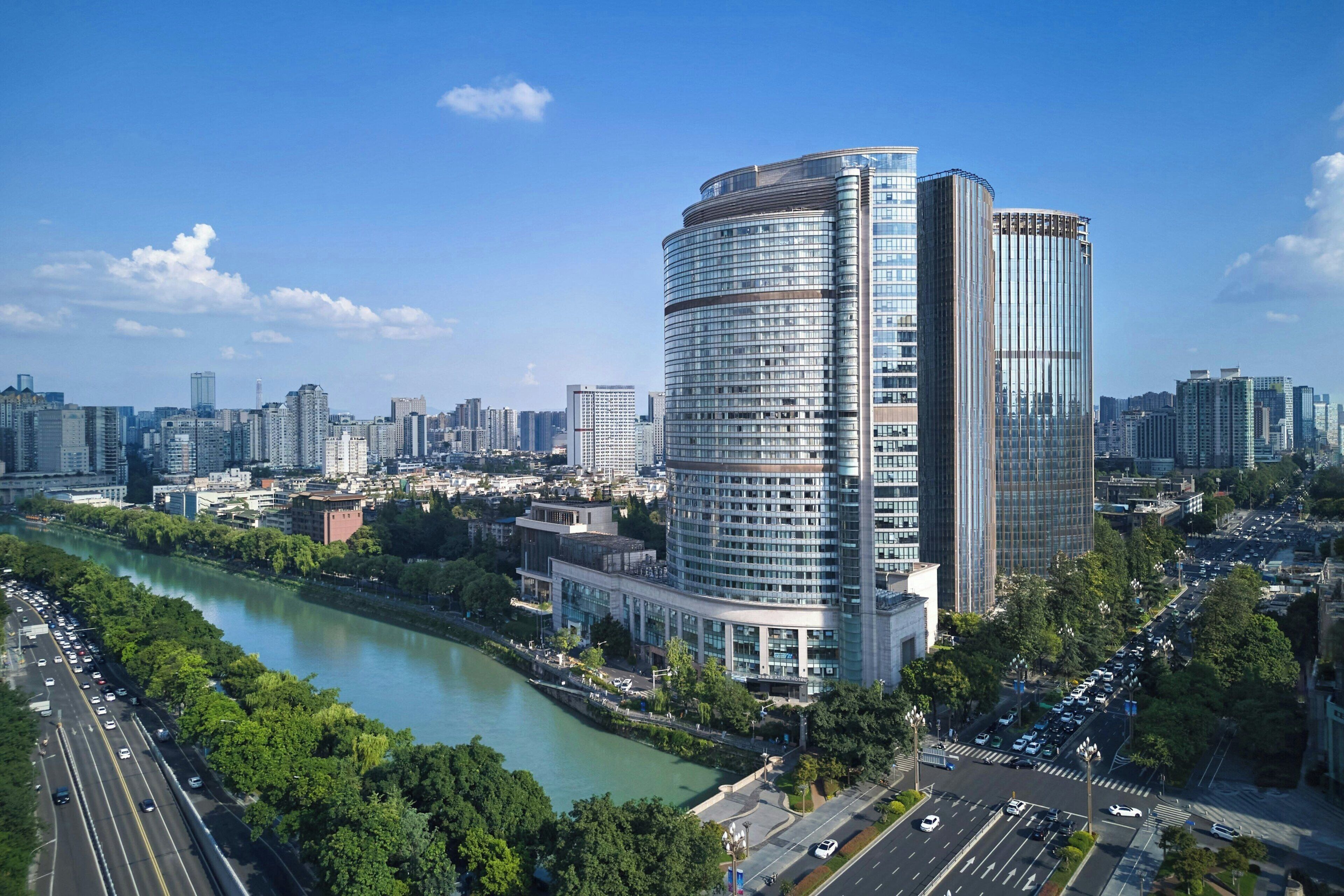 A high-rise building with a curved facade, surrounded by a river and a busy road.