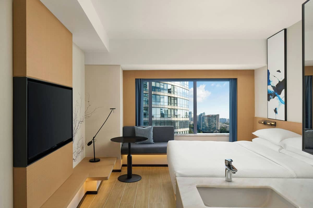 A modern hotel room with a large bed, a TV, a small table, and a sofa.