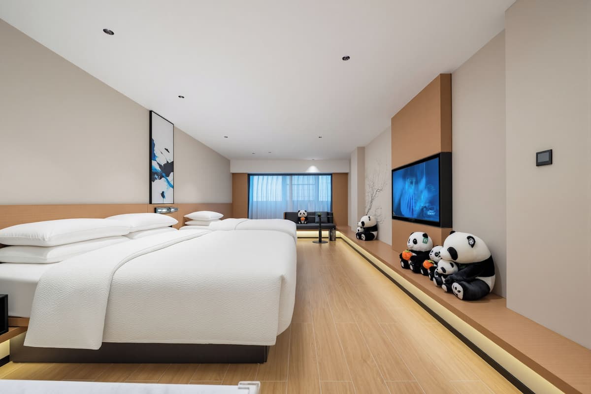 A modern hotel room with a large bed, a TV, and decorative panda figures.