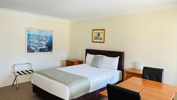 Habitación de hotel con cama, una mesa y una silla. Se observa un cuadro en la pared y un marco de fotos.