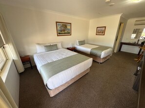 A hotel room with two single beds, a small desk, a chair, a mirror, and a window.