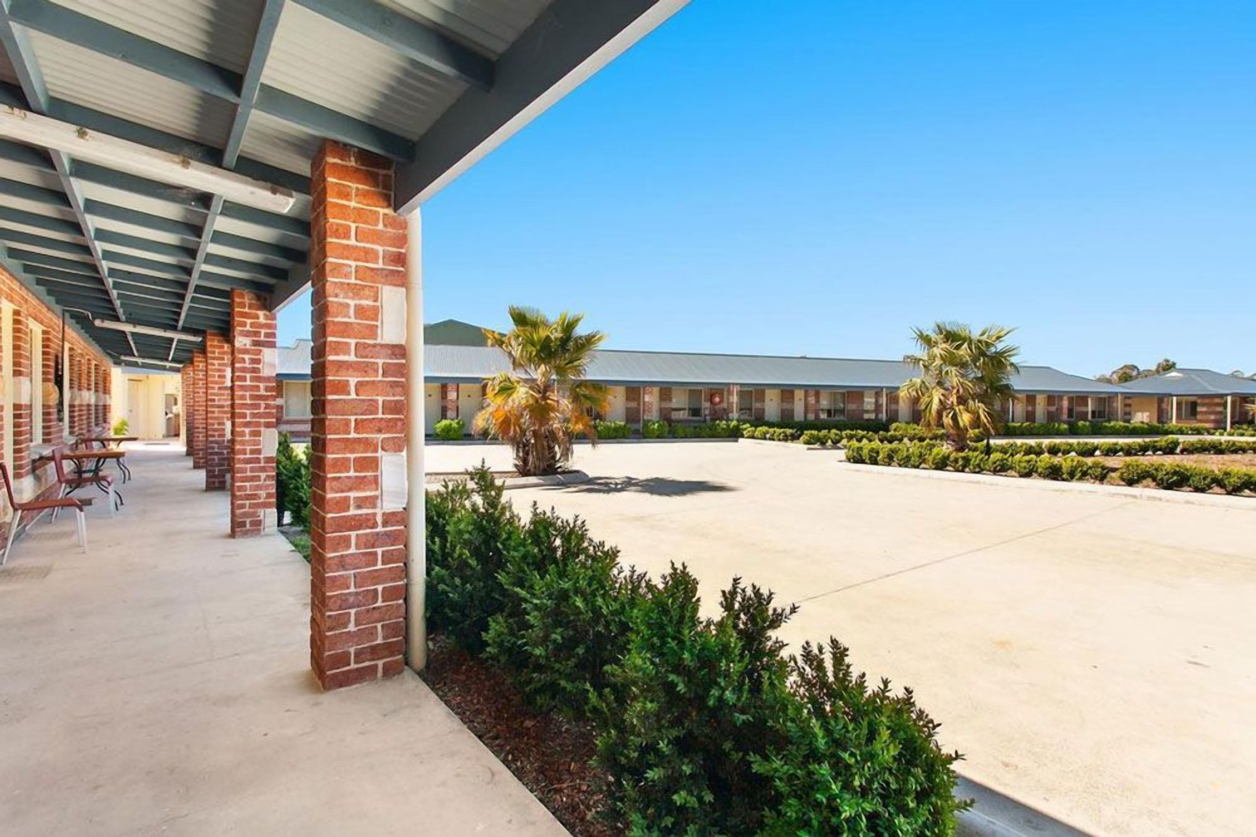 A covered outdoor area with brick pillars, a paved walkway, and a building in the background.