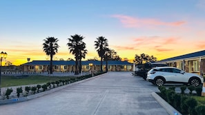 Un hotel con un largo camino de entrada, palmeras y un coche blanco estacionado al costado.