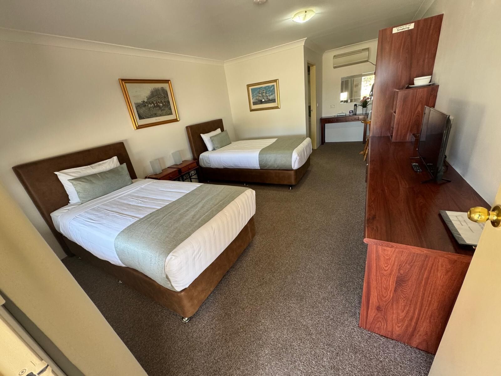 Habitación de hotel con dos camas, un escritorio de madera y una televisión.