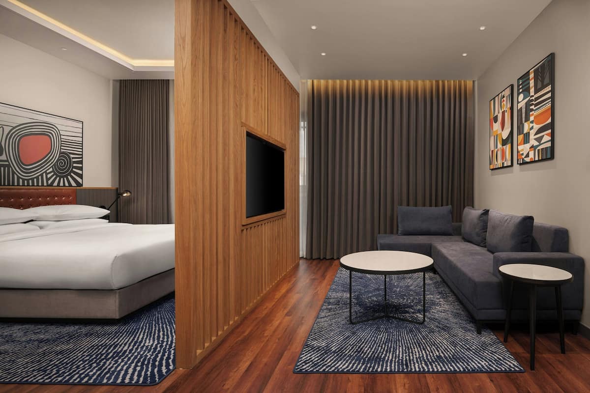 A modern hotel room with a bed, a sofa, a TV, and artwork on the walls.