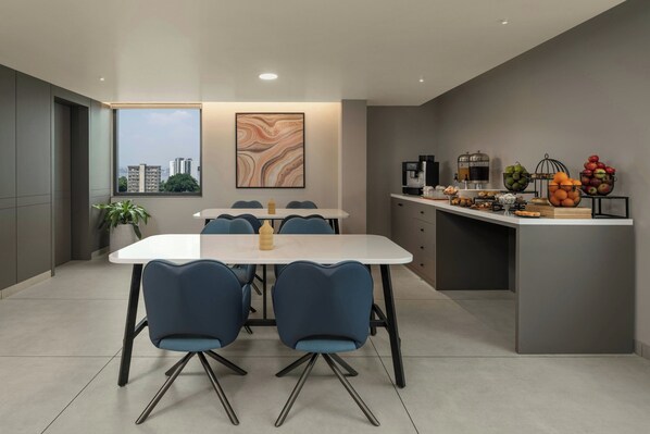 Une cuisine moderne avec un coin repas, comprenant une table blanche, des chaises bleues et une vue sur la ville grâce à une grande fenêtre.