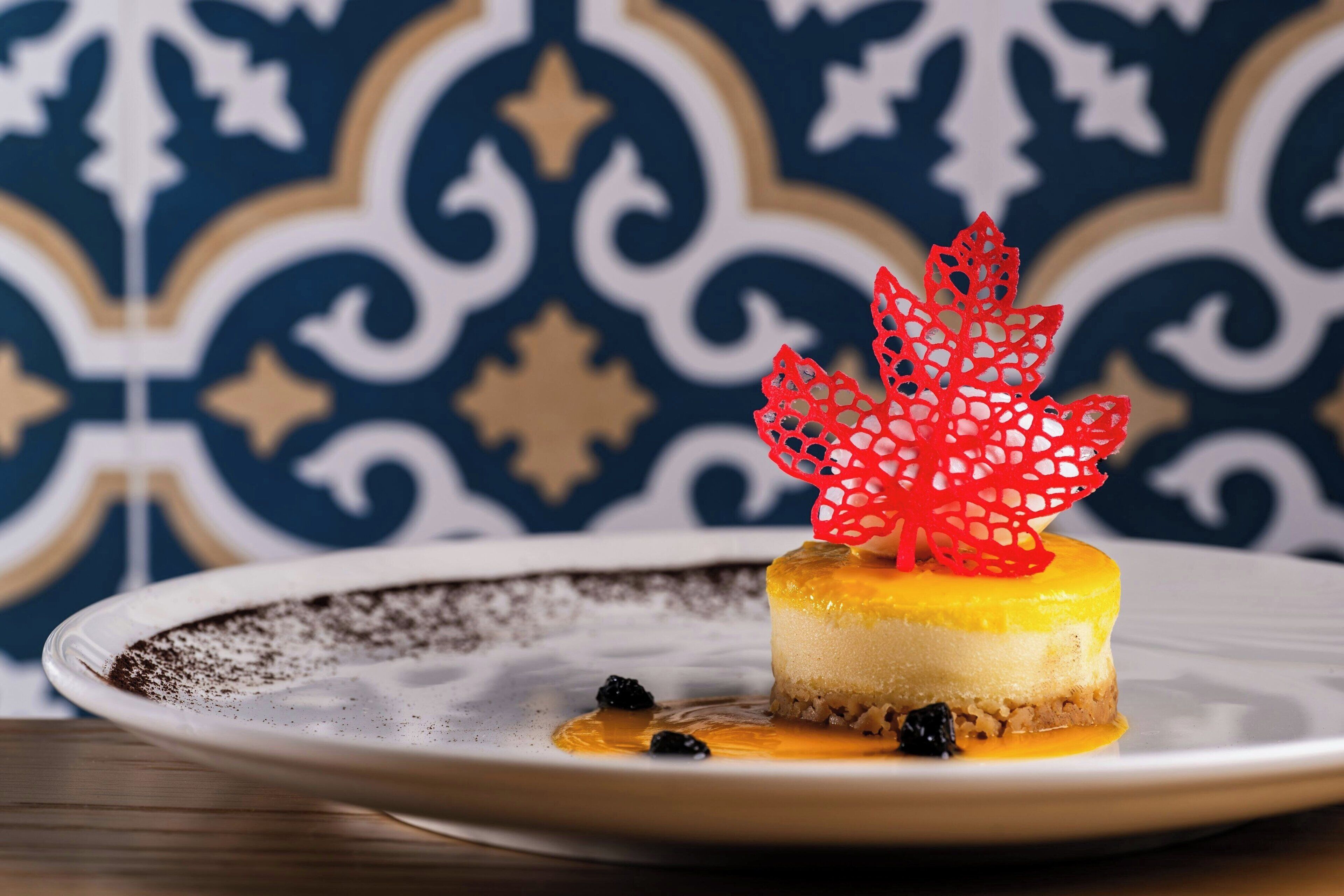 A dessert on a plate with a decorative leaf and berries, set against a patterned background.