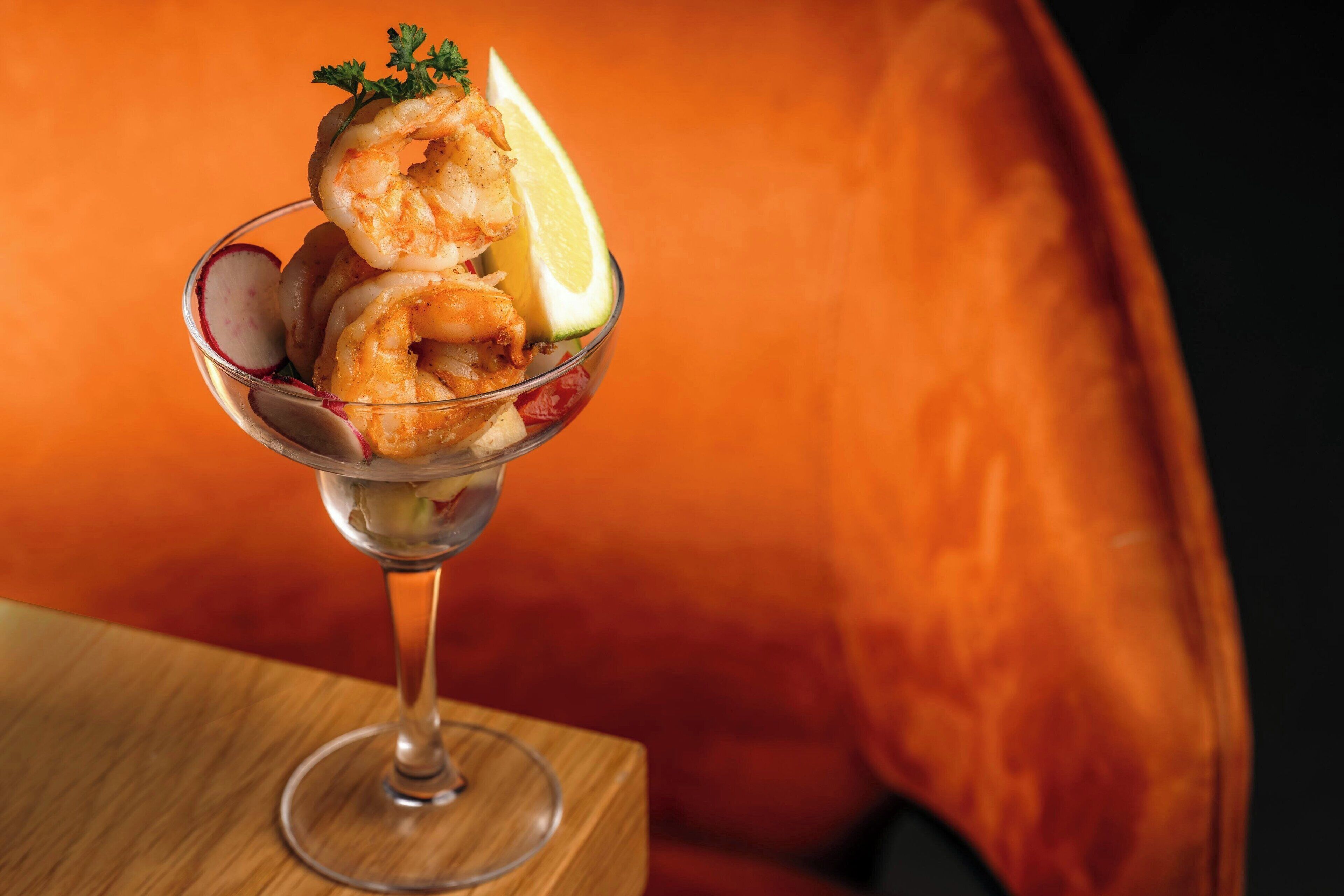 A shrimp cocktail in a glass with lemon and radish garnish.