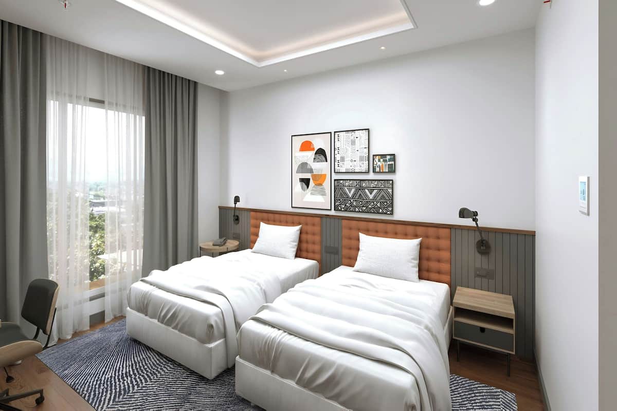 A hotel room with two beds, a desk, a chair, a window with curtains, and artwork on the wall.