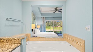 Bagno d'albergo con una vasca da bagno ampia, un ventilatore a soffitto e vista su un campo da golf attraverso una finestra.