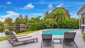 A poolside area with lounge chairs and a view of a lake and greenery. - Luxe Coastal Escape King BD Heated pool WaterFront (Pompano Beach)