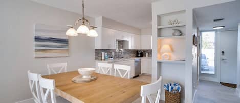 Una cocina moderna con armarios blancos, una mesa de comedor de madera y una lámpara colgante.