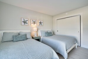 A bedroom with two beds, a nightstand with a lamp, and three starfish wall art pieces.