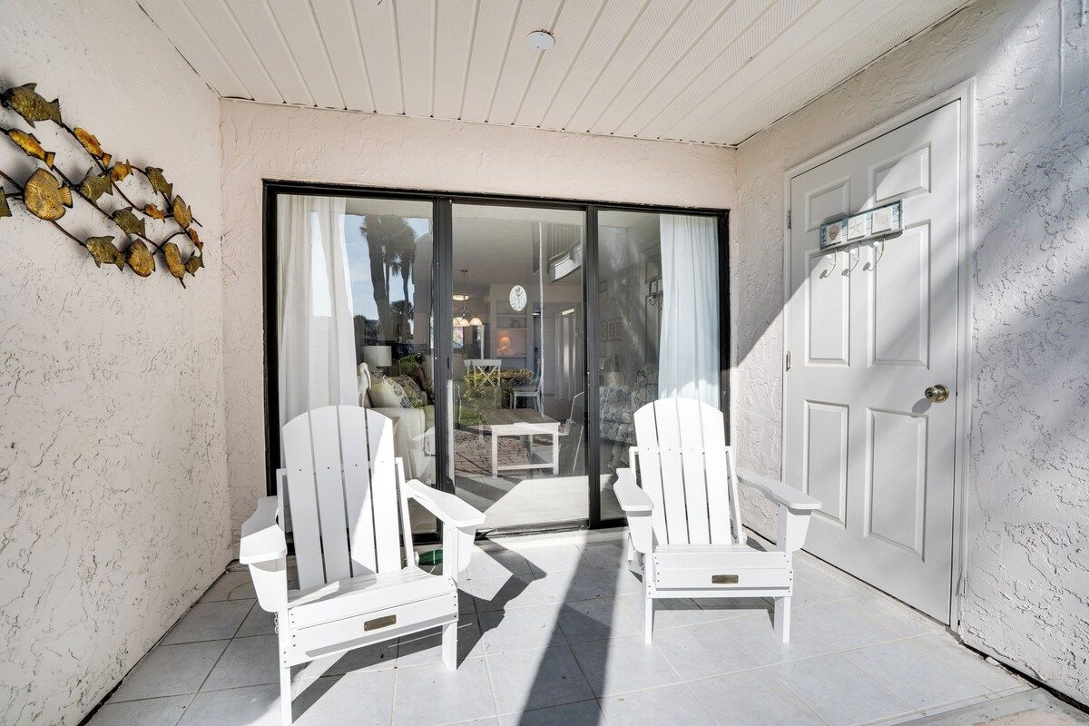 A covered patio area with two white Adirondack chairs, a white door, and a glass sliding door leading to an indoor space.
