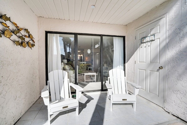 A covered patio area with two white Adirondack chairs, a white door, and a glass sliding door leading to an indoor space.