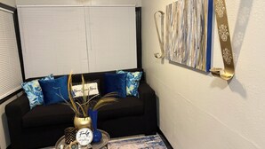 A living room with a black sofa, blue pillows, a small round table with a decorative item, and a wall-mounted art piece. - Charming and Cozy Winter Haven Oasis (Winter Haven)