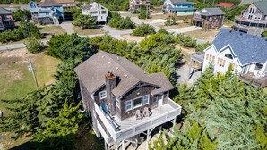 A multi-story house with a large porch and a chimney, surrounded by trees and other houses. - Cozy Dog-Friendly Getaway | Hot Tub & Beach Access (Waves)