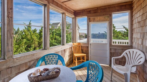 A covered patio with wooden walls, large windows, and two blue chairs. - Cozy Dog-Friendly Getaway | Hot Tub & Beach Access (Waves)