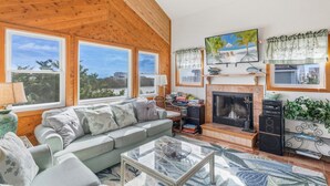 A cozy living room with a fireplace, large windows, and a comfortable seating area. - Cozy Dog-Friendly Getaway | Hot Tub & Beach Access (Waves)