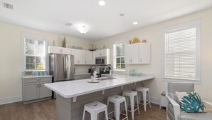 A modern kitchen with a large island, white cabinetry, stainless steel appliances, and a seating area with a gray sofa and bar stools.