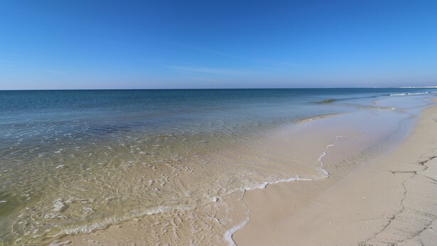 A beach with clear water, a sandy shore, and a clear sky.