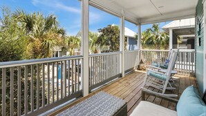A covered outdoor deck with a wooden floor, white railings, and a rocking chair with blue cushions.