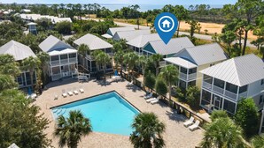 A resort with multiple two-story buildings, a central swimming pool, and a view of the ocean.