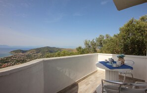 Een balkon met een tafel gedekt voor twee, met uitzicht op een kustplaatsje en heuvels.