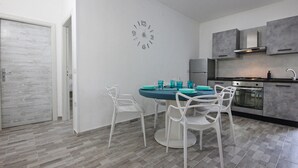 A modern kitchen with grey cabinets, a stainless steel stove, and a round table with white chairs. - Lovely apartment in Castellabate (Castellabate)
