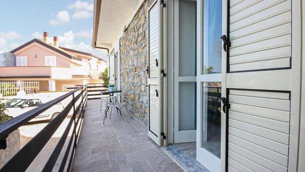 A balcony with a stone wall, a table with chairs, and a car parked in the background. - Lovely apartment in Castellabate (Castellabate)