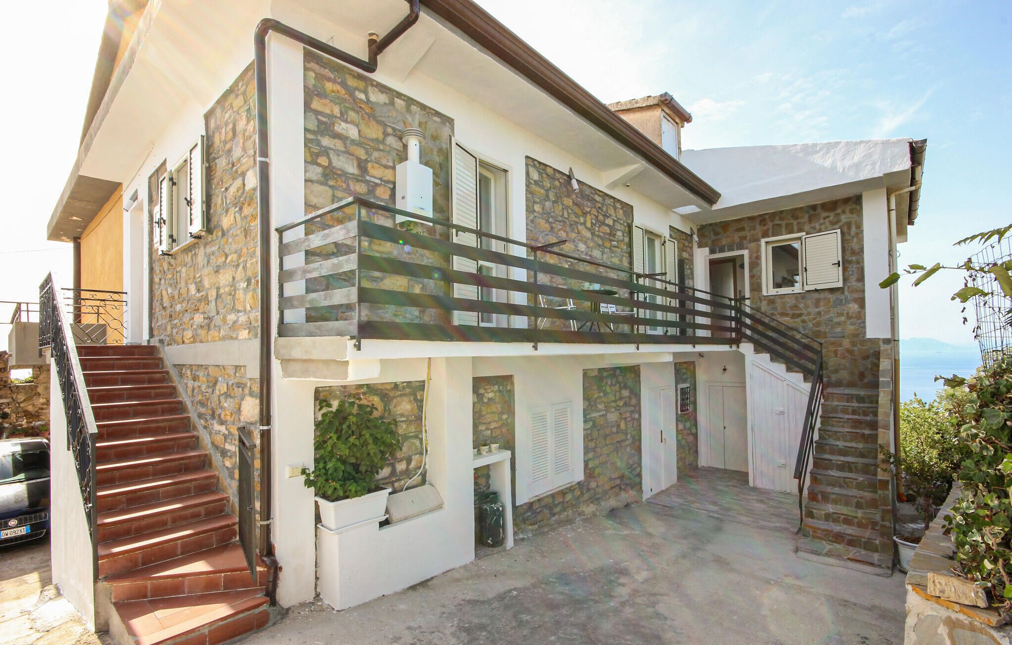 Uma casa de dois andares com fachada de pedra, uma varanda e uma escadaria que leva ao andar superior.