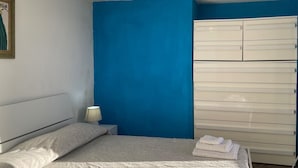 Quarto com cama, mesa de cabeceira, abajur e guarda-roupa branco.