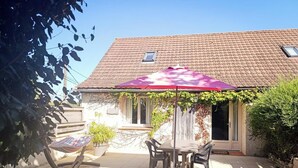 Une terrasse avec une table et des chaises, un parasol rouge et une maison avec un toit en tuiles.